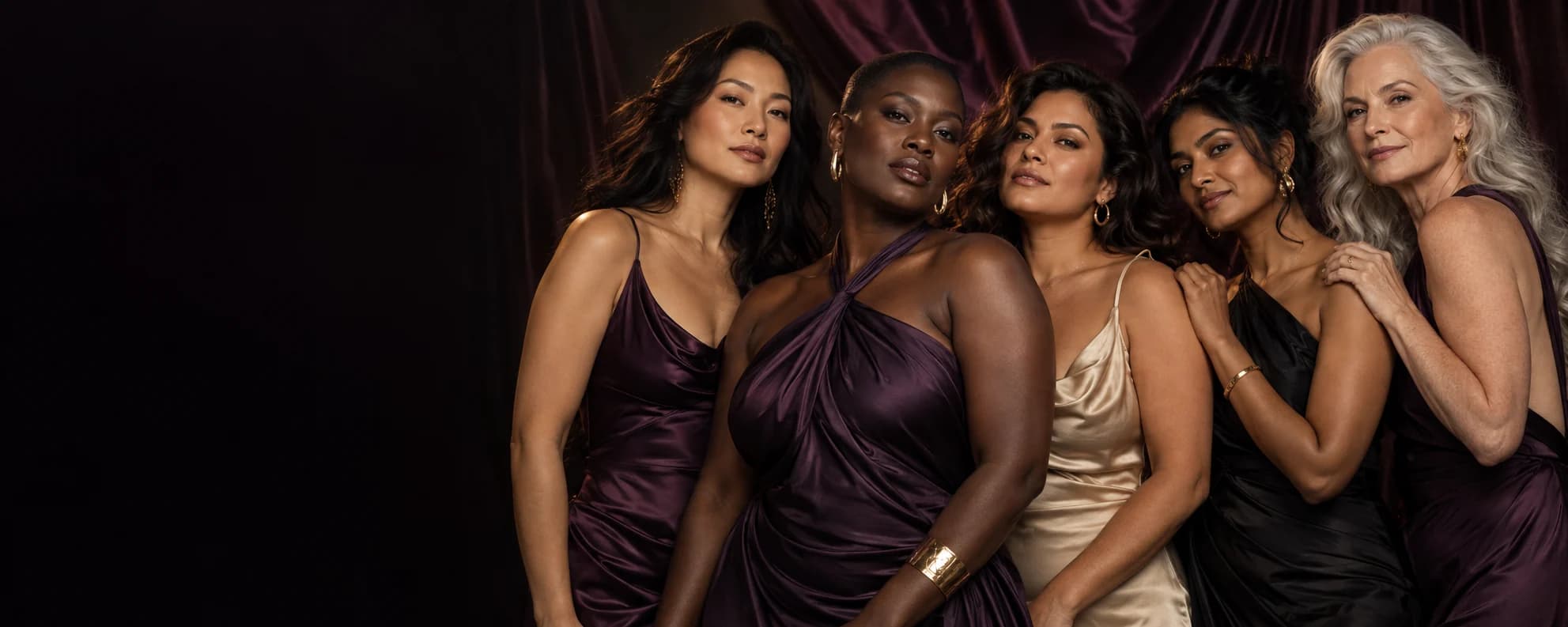 Five adult women of different ages and skin tones wearing elegant purple, black and champagne dresses.