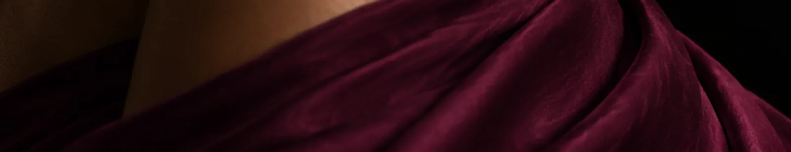 A woman in a flowing plum silk dress in soft light.